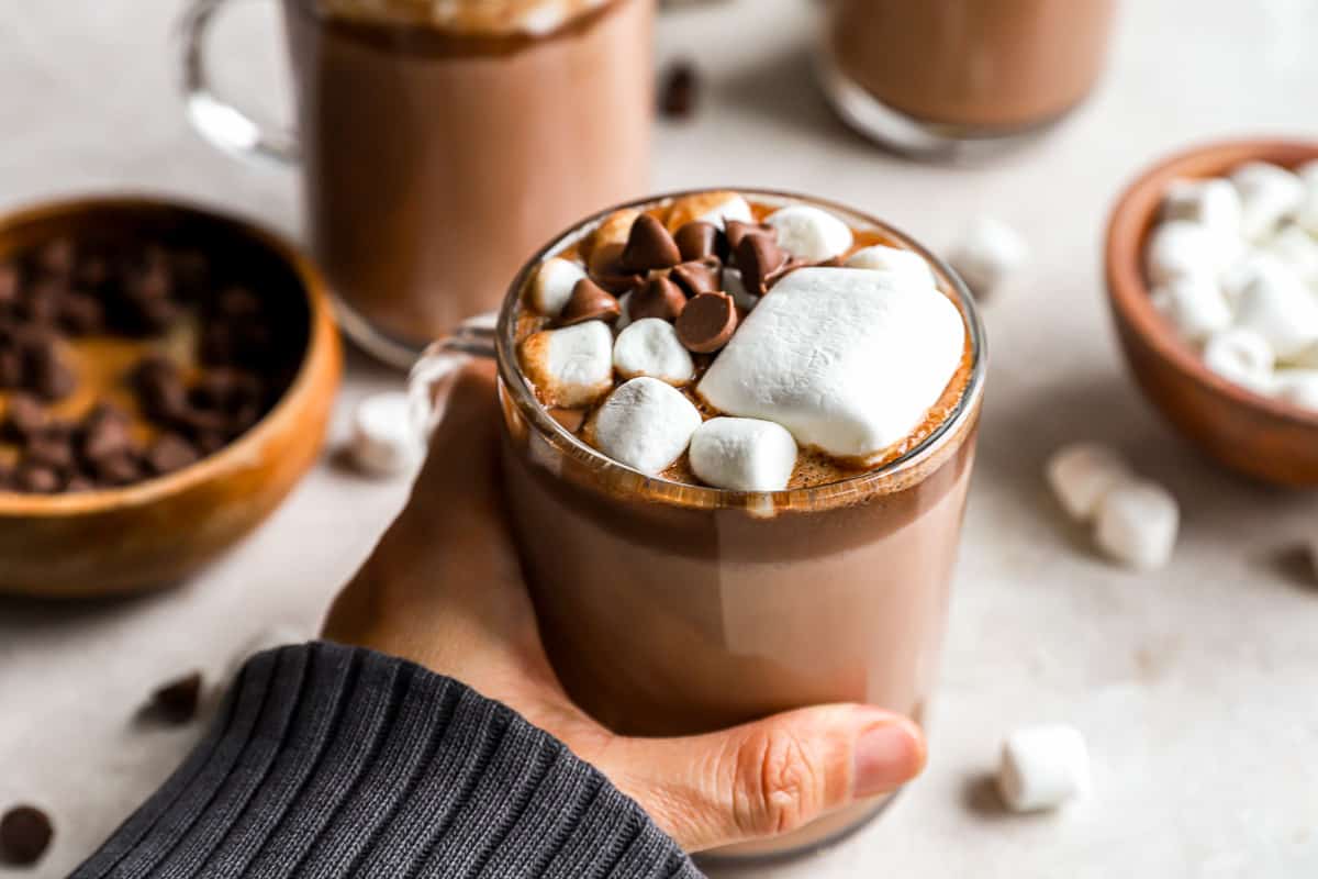 Uma pessoa segurando uma xícara de chocolate quente Crockpot com marshmallows.