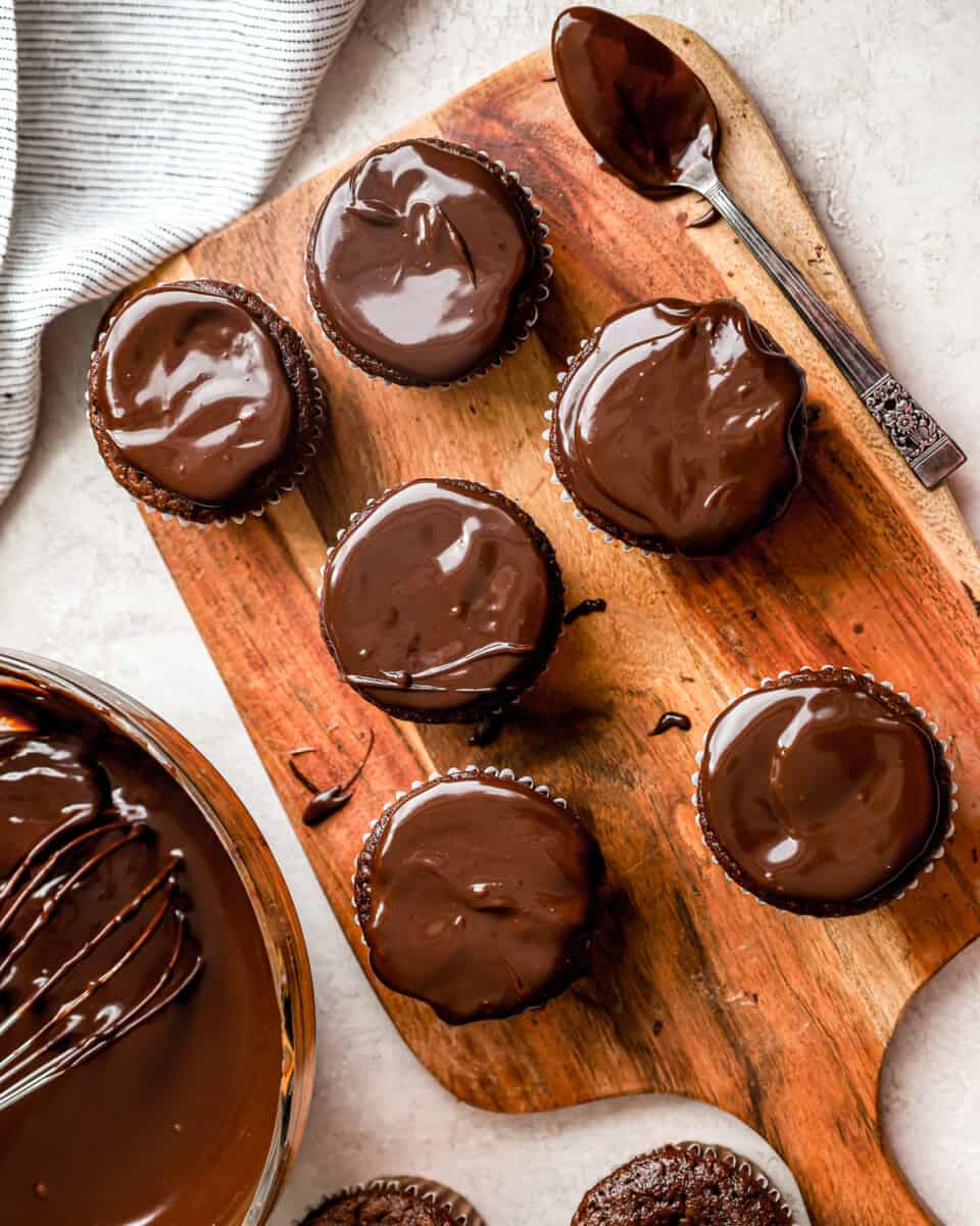 Cupcakes cobertos com ganache de chocolate sobre uma tábua com uma colher.