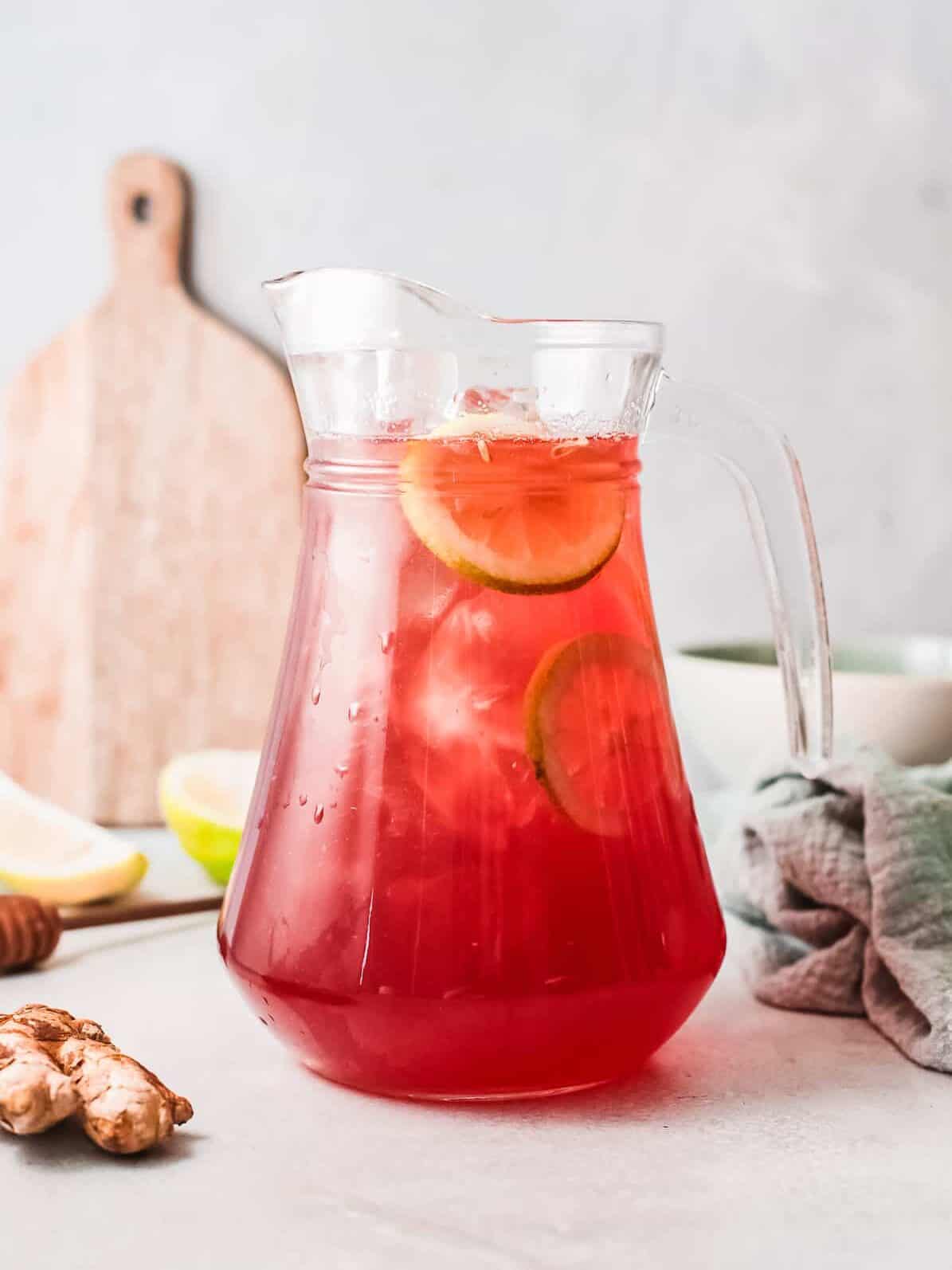 uma bebida vermelha em uma jarra com rodelas de limão e gelo.