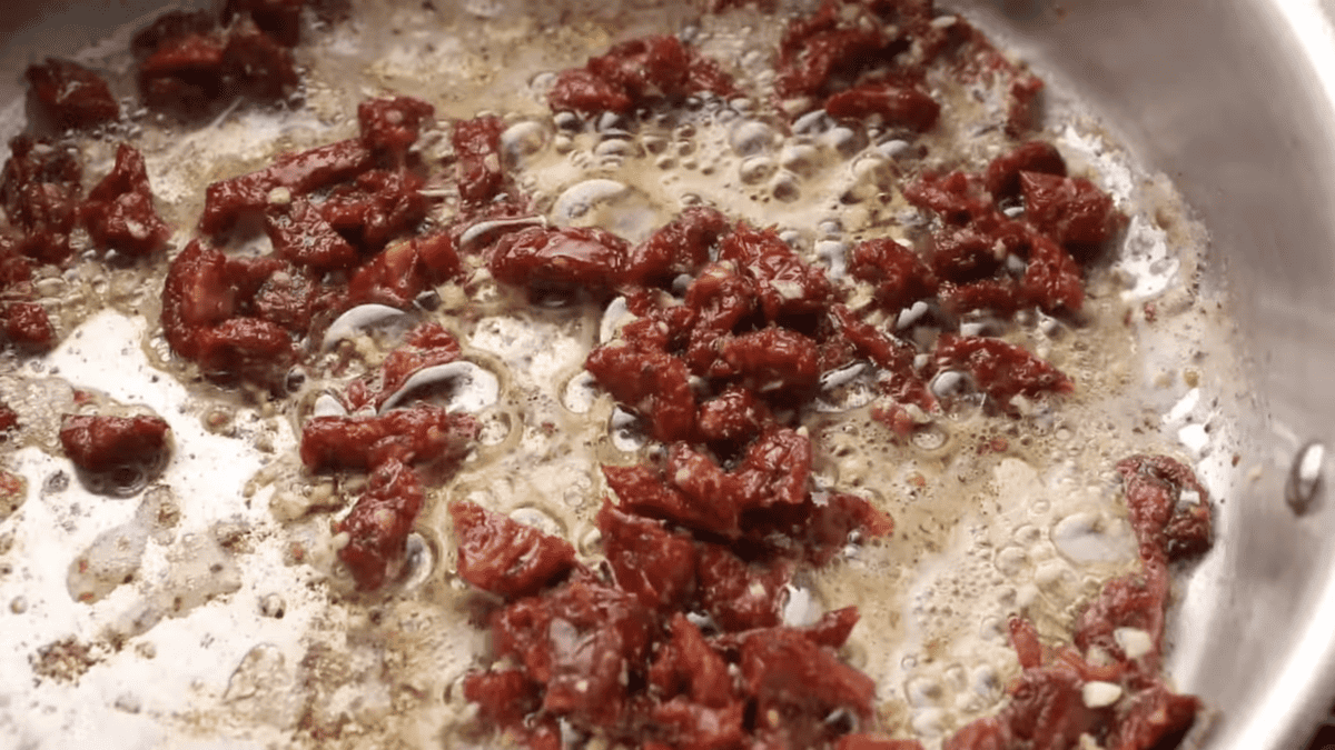 Frango toscano sendo cozido em uma panela cheia de tomates secos embebidos em óleo.