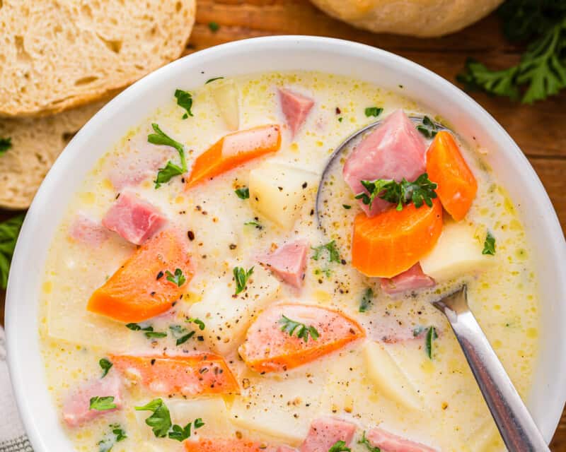Uma tigela de sopa com cenoura, batata e presunto.