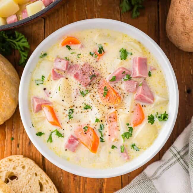Uma tigela de sopa com batata, cenoura e presunto.
