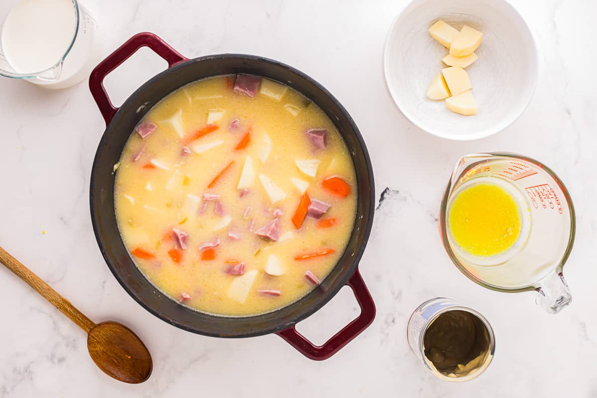 Uma panela de sopa com cenoura, batata e presunto.