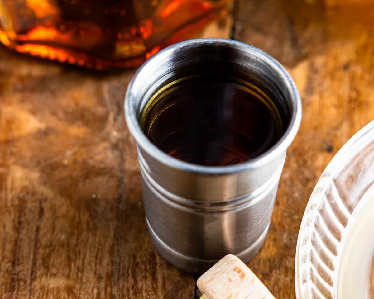 Uma garrafa de bourbon está sobre uma mesa ao lado de uma xícara de café.