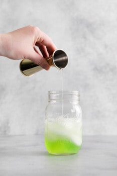 suco de limão adicionado ao licor de maçã, vodka e xarope simples em um frasco de vidro com gelo.