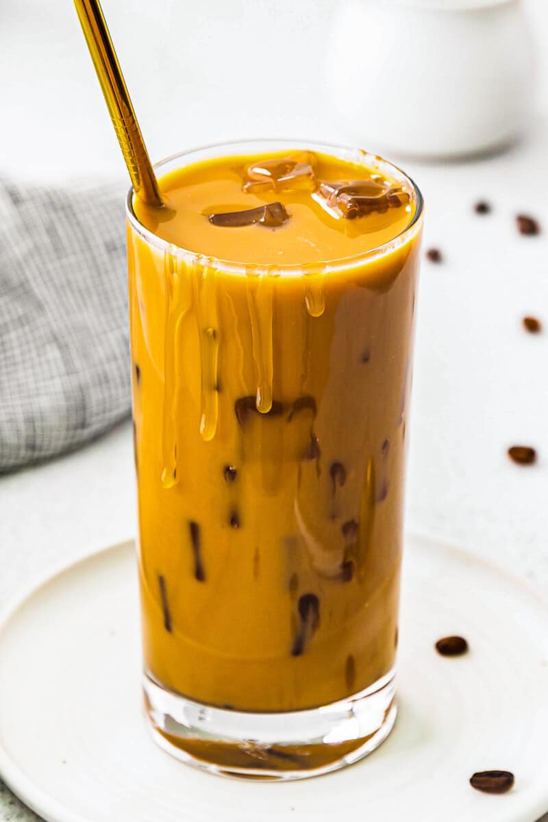 de perto, café com leite de caramelo gelado mexido em copo com canudo dourado