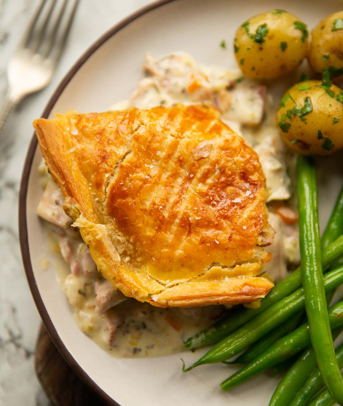overhead shot of chicken and ham pie served on white plate with potatoes and green beans