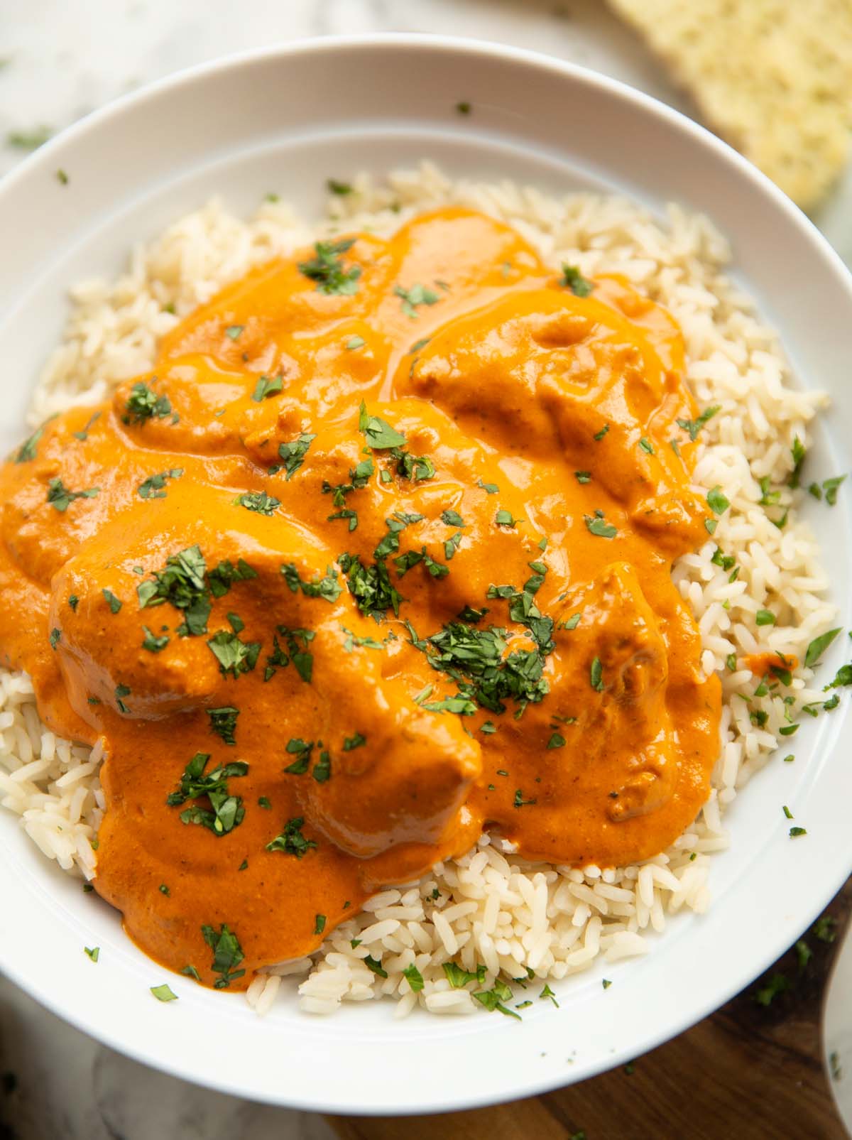 close up shot of homemade butter chicken served on rice in large white bowl