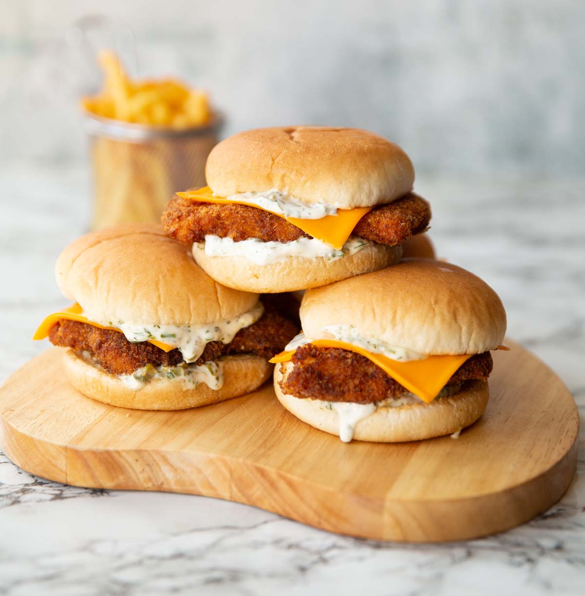 3 homemade filet-o-fish stacked on each other on wooden board with fries in the background