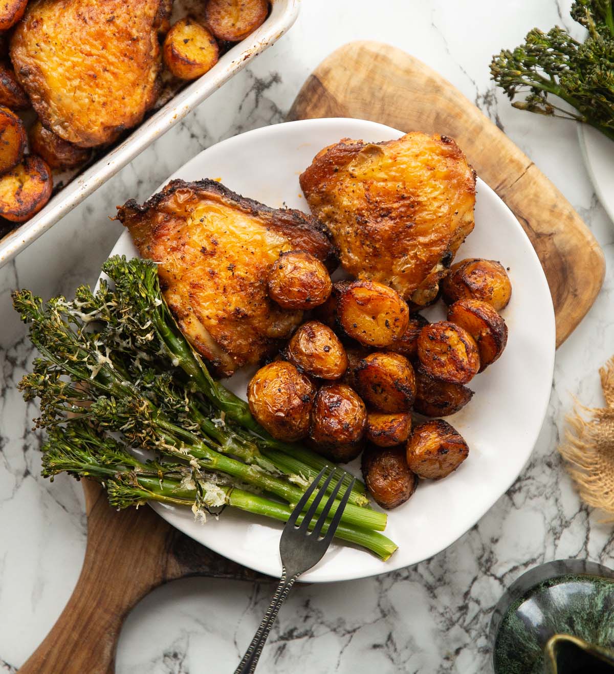 overhead shot of baked chicken and potatoes served on small white plate with tenderstem broccoli