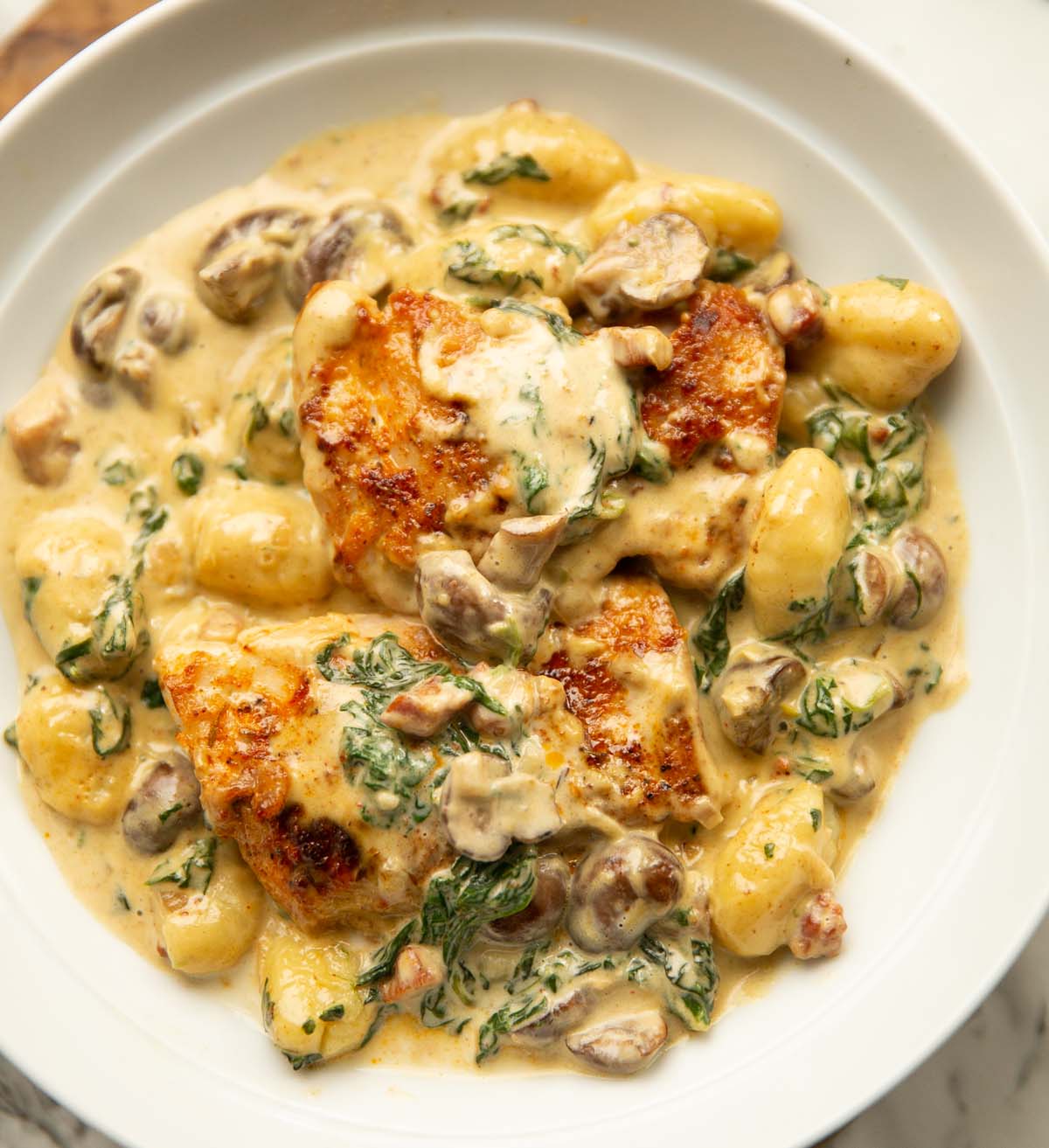 close up shot of creamy chicken with gnocchi in large white bowl