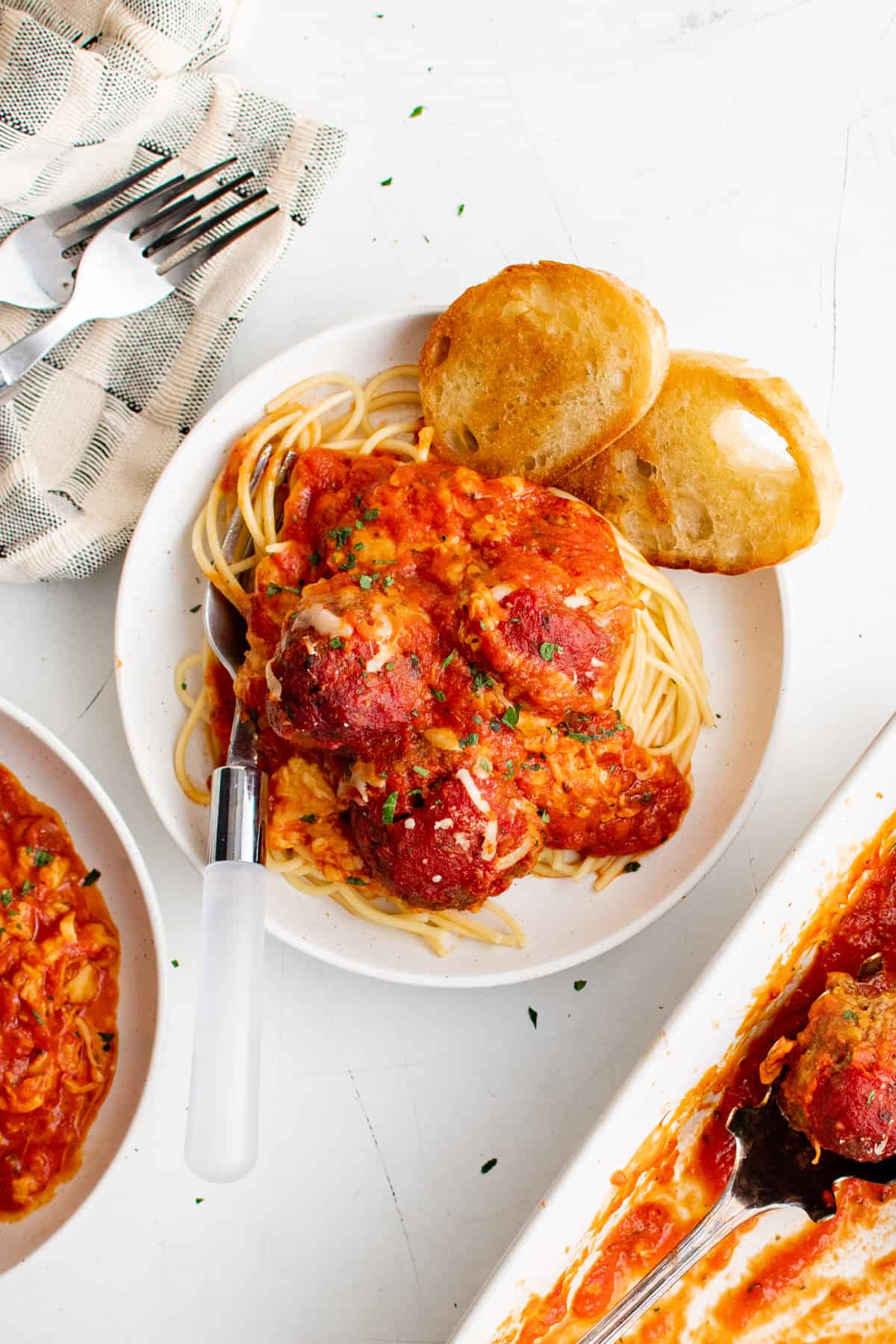 um prato de caçarola de espaguete e almôndegas em um prato, cercado por mais tigelas e travessas.