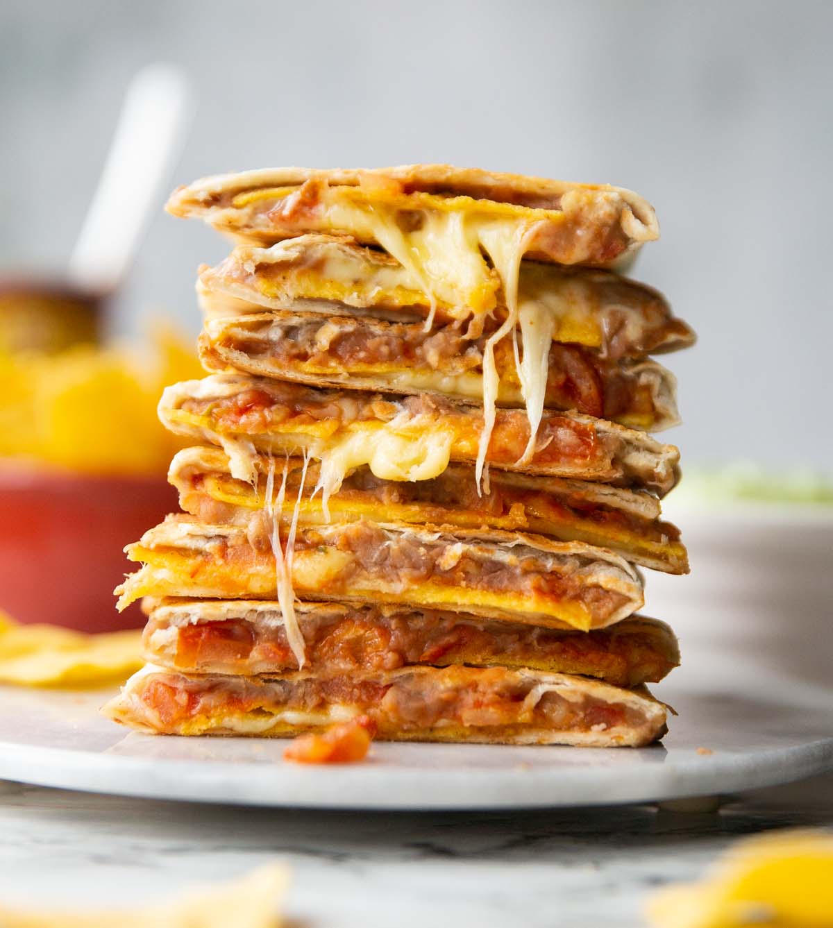 8 refried bean quesadillas halves stacked on each other on marble plate with ingredients blurred in background