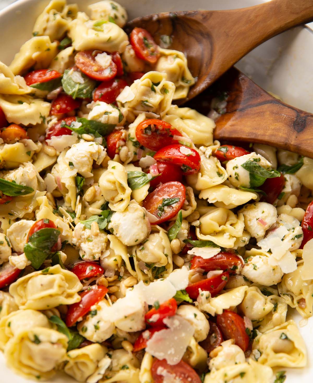 tortellini pasta salad in large white bowl with salad tossers at the back