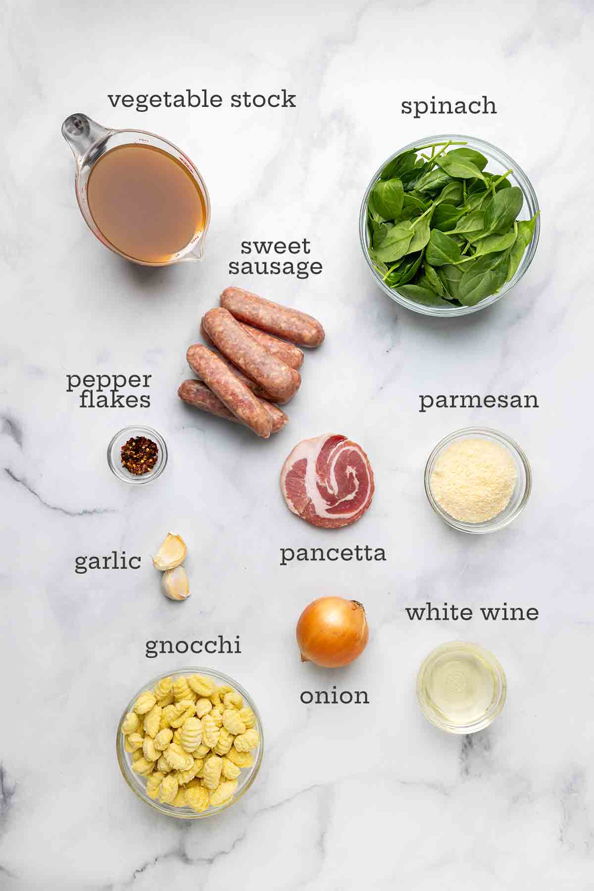 Ingredientes para sopa de linguiça italiana - caldo, espinafre, linguiça, pimenta em flocos, pancetta, parmesão, cebola, nhoque, vinho branco e alho.