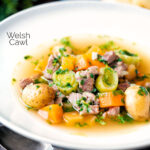 Welsh cawl, uma sopa à base de caldo de cordeiro e vegetais em uma tigela branca com uma sobreposição de título.