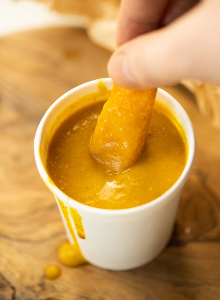 dedos mergulhando uma batata frita em um pequeno pote de molho de curry de loja de batatas fritas
